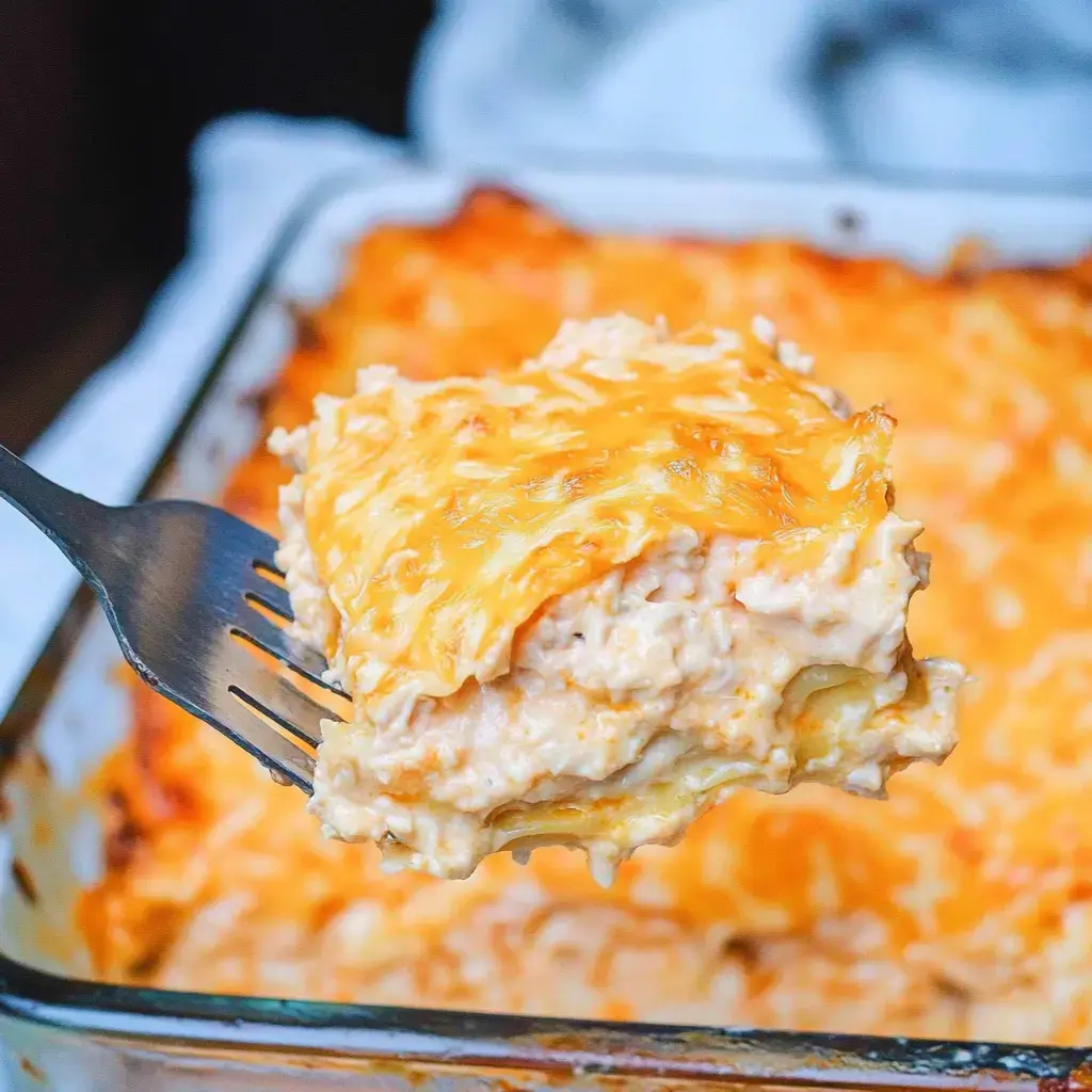 A cheesy pasta serving lifted out of a baking dish with golden-topped cheese.