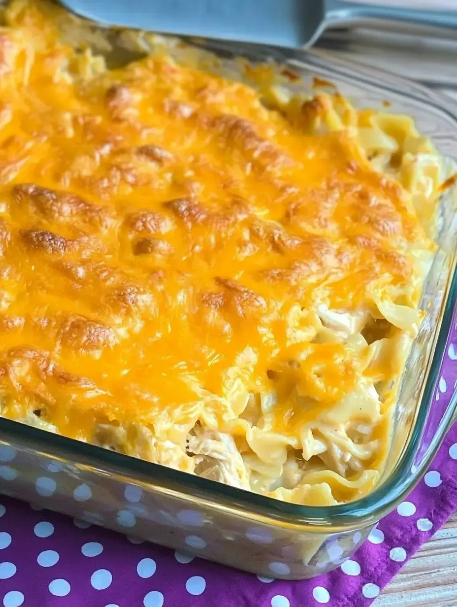 A close-up view of a baked pasta casserole topped with melted cheese in a glass dish on a purple polka-dotted cloth.