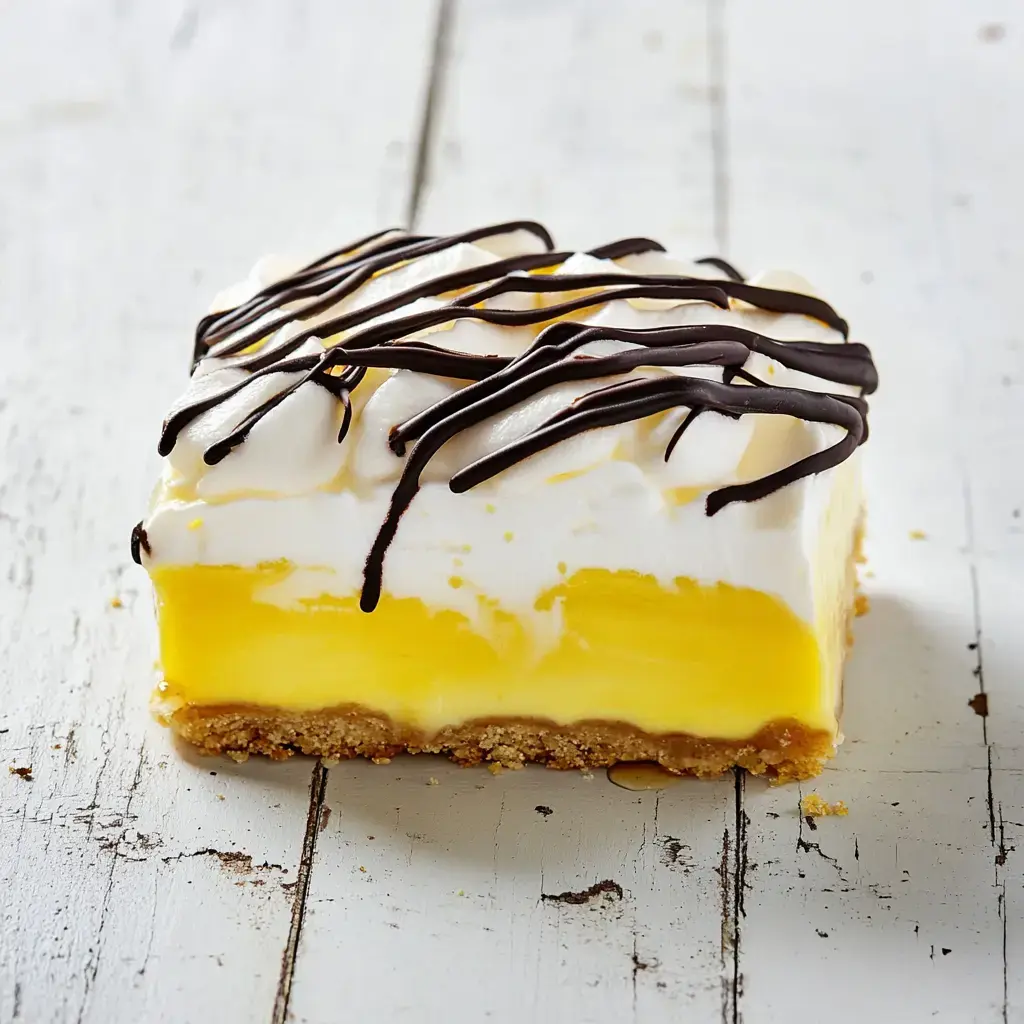 A creamy dessert slice with whipped topping and chocolate drizzle on a rustic white wooden table.