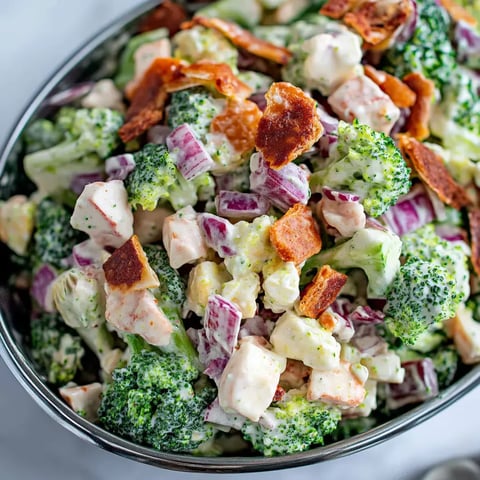 A bowl packed with broccoli, bacon, red onions, and cheese cubes.